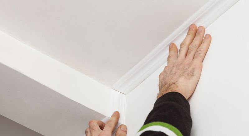 Mains ajustant une moulure de plafond blanche dans l'angle d'une pièce.