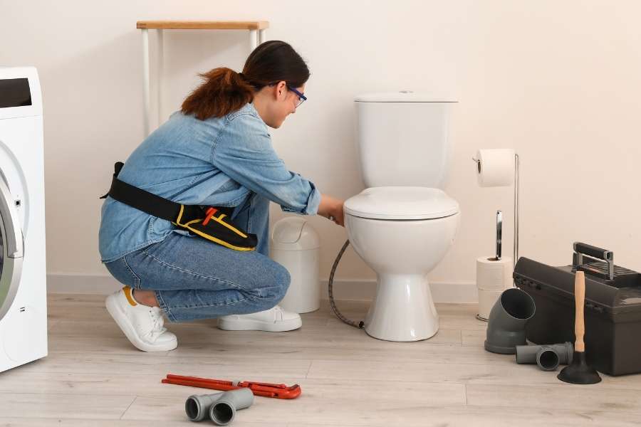 Femme plombier accroupie en train d'installer des toilettes avec des outils pour aménager des toilettes