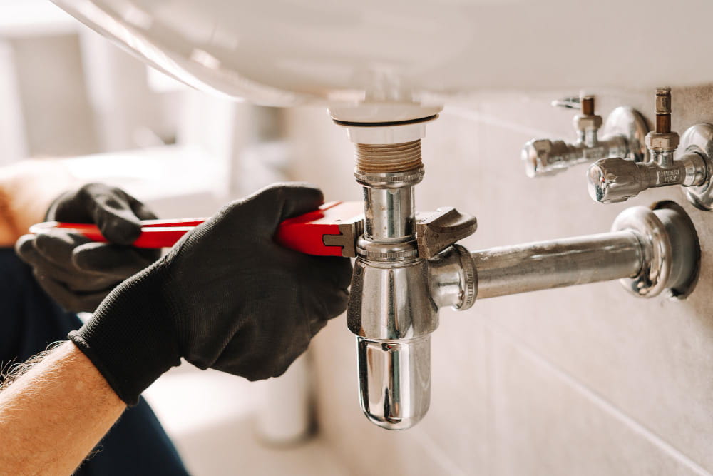 Main d'un plombier Gex serrant un siphon de lavabo chromé avec une clé à molette rouge