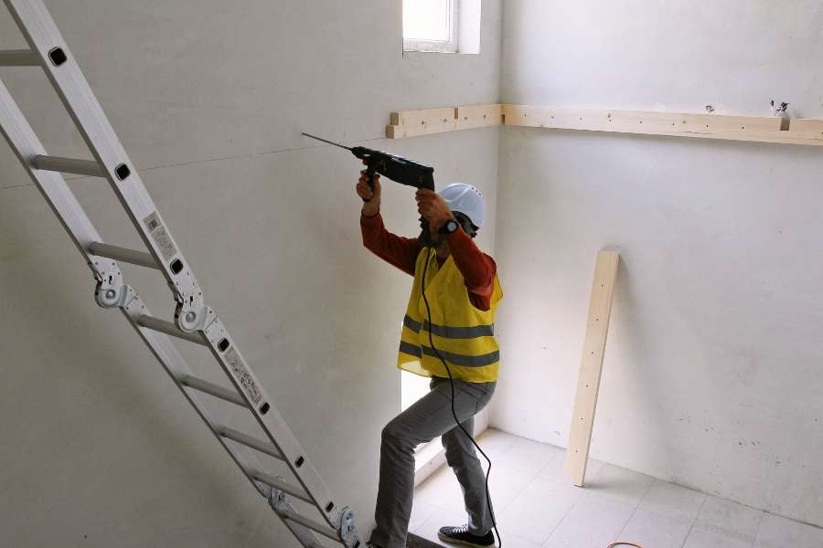 Ouvrier en train d'aménager une mezzanine en perçant un mur avec une perceuse sur échelle