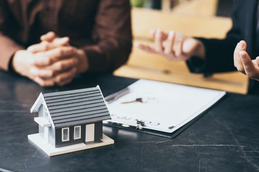 Des personnes discutent autour d'un contrat et d'une maison miniature pour préparer l'achat d'un bien en copropriété.