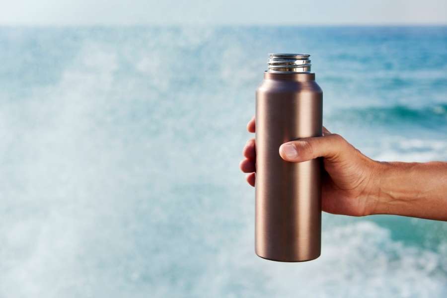 Une main d'homme tient une gourde filtre à eau en acier inoxydable devant l'océan.