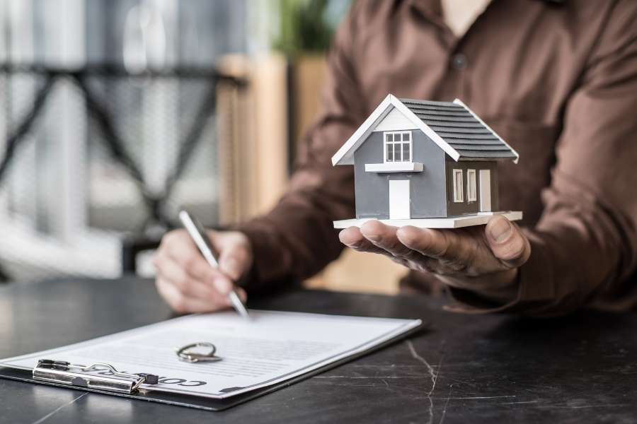 Un investisseur signe le contrat pour son premier investissement locatif en tenant une maquette de maison.