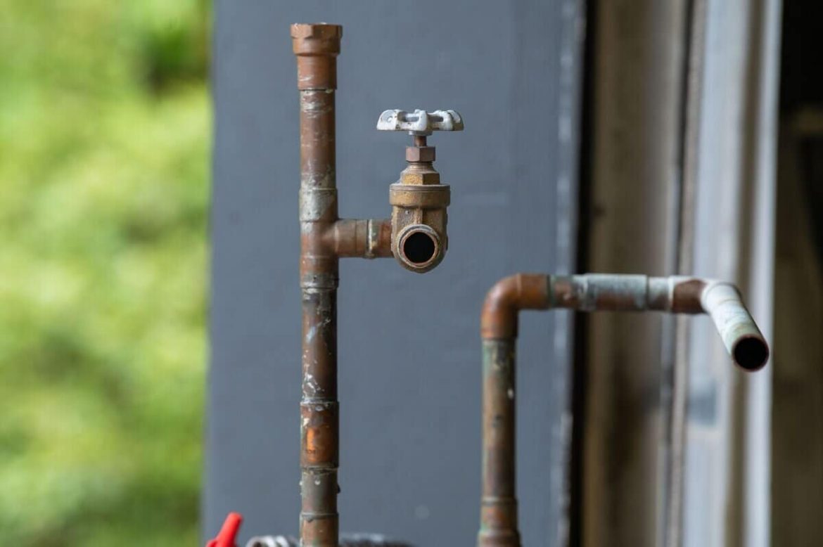 Gros plan sur une tuyauterie en cuivre ancienne où se trouve une vanne, montrant des signes de corrosion pouvant mener à une fuite d'eau.