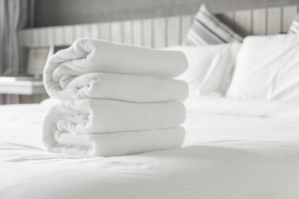 Pile de serviettes blanches moelleuses posée sur un lit double propre et bien fait.