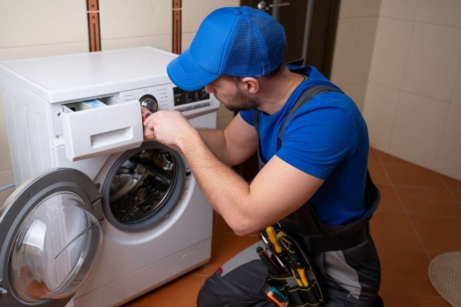 Un technicien en tenue professionnelle effectue la réparation Whirlpool d'une machine à laver.