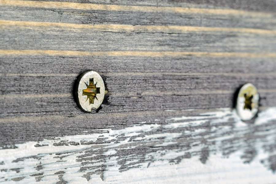 Gros plan sur deux têtes de vis métalliques visibles sur une planche en bois vieilli.